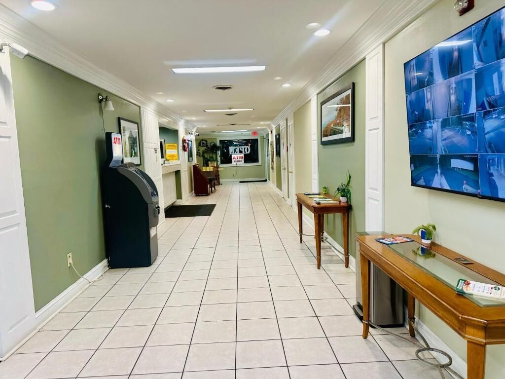 A hotel lobby with a tiled floor, an ATM, a reception desk, and a large security monitor.