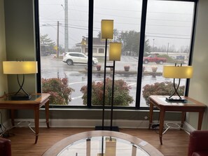 A room with a large window, two standing lamps, and a wooden table. - Astoria North Extended Stay (Danville)