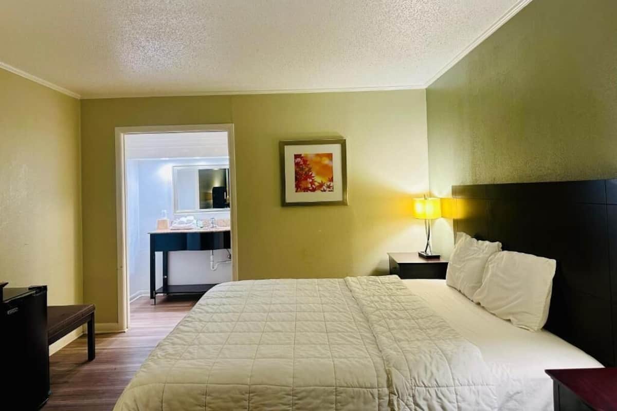 Ein Hotelzimmer mit Bett, Nachttisch, Lampe und einem durchgegangenen Tür zu sehendem Badezimmer.