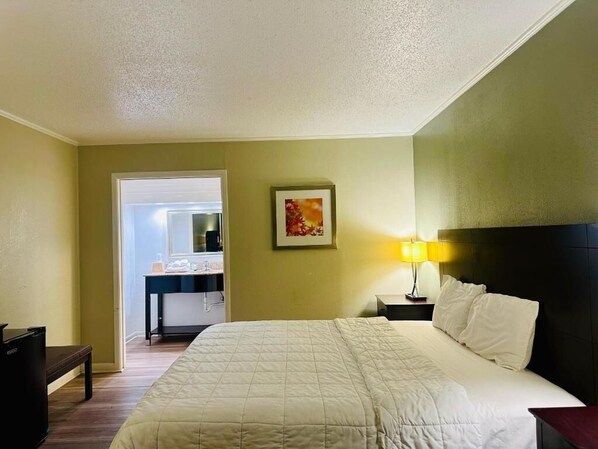 A hotel room with a bed, bedside table, lamp, and a bathroom visible through an open door. - Astoria North Extended Stay (Danville)
