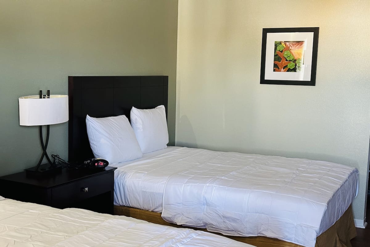 Ein Hotelzimmer mit zwei Betten, einem Nachttisch mit Lampe und einem gerahmten Bild an der Wand.