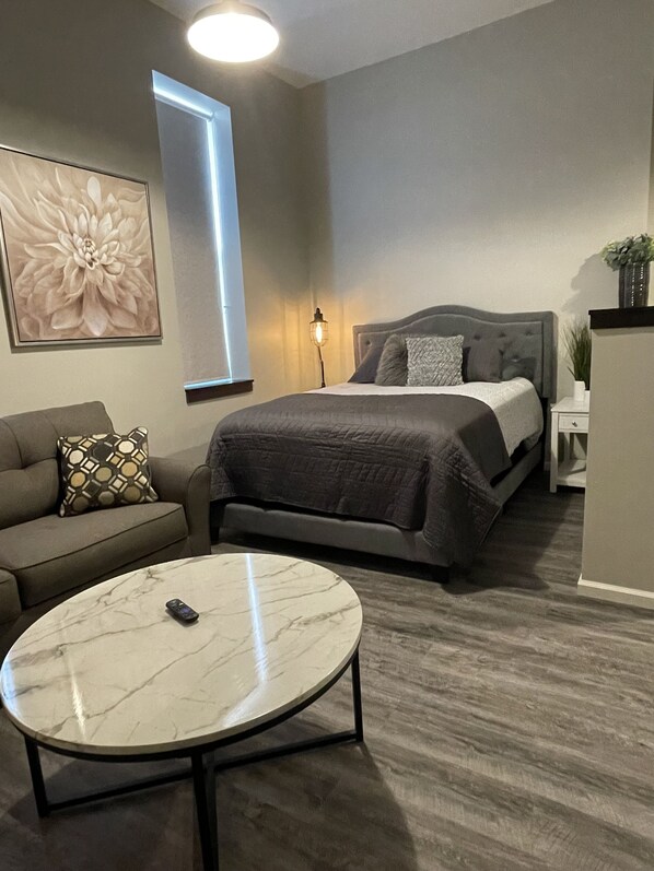 A modern bedroom with a bed, a sofa, a coffee table, and a large floral artwork on the wall.