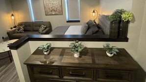 Una sala moderna con un sofá, una mesa de centro y un mueble de madera oscura. Hay dos lámparas fijadas a la pared y un cuadro sobre el sofá.