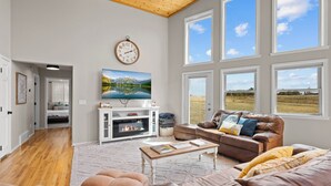 A spacious living room with a fireplace, large windows, and a view of the outdoors. - 20 ft swim spa! 5 bed, 4 bath, hot tub, 5 acres, game room, north CO Springs! (Colorado Springs)