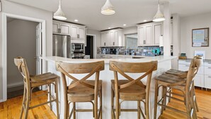 A modern kitchen with white cabinets, stainless steel appliances, and wooden bar stools. - 20 ft swim spa! 5 bed, 4 bath, hot tub, 5 acres, game room, north CO Springs! (Colorado Springs)