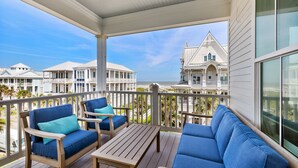 A wooden deck with blue furniture, a table, and a view of a coastal building.