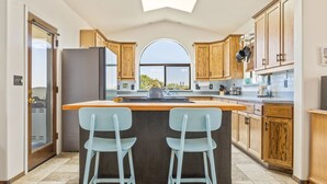 Une cuisine moderne dotée d’un îlot central, de deux tabourets de bar, de meubles en bois et d’une grande fenêtre.