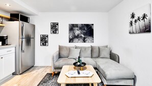 A modern living space with a grey sofa, a wooden coffee table, and a kitchen area with a stainless steel refrigerator. - Spacious 1BR Near Downtown & Water w/ Full Kitchen (Lake Worth)