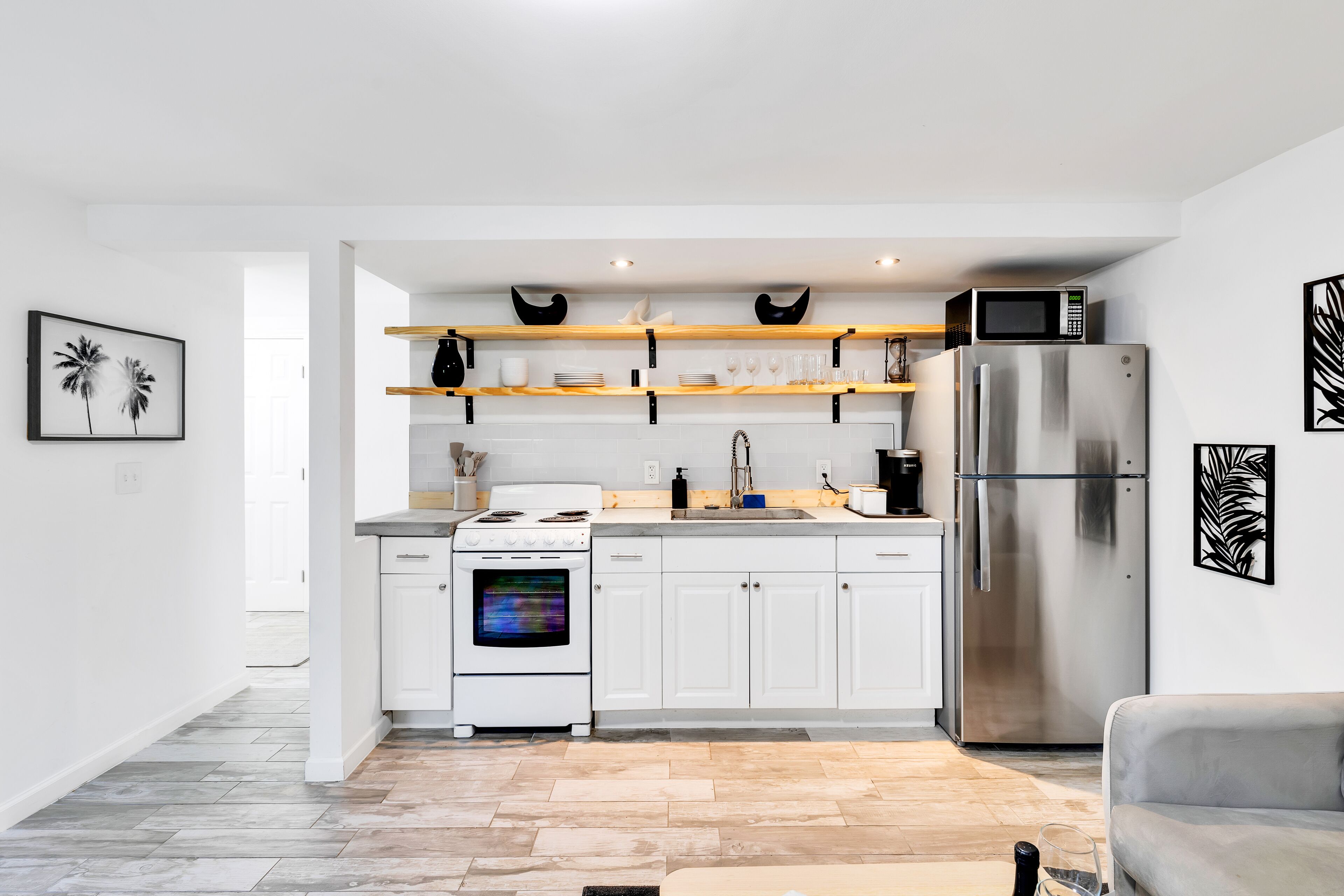 A modern kitchen with white cabinetry, a stainless steel refrigerator, a microwave, and wooden shelves above the counter.