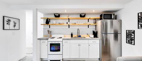 A modern kitchen with white cabinetry, a stainless steel refrigerator, a microwave, and wooden shelves above the counter.
