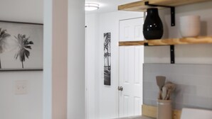A hallway with a white door, a black vase on a shelf, and a framed picture on the wall. - Spacious 1BR Near Downtown & Water w/ Full Kitchen (Lake Worth)