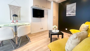 A modern living room with a flat-screen TV mounted on the wall, a dining area with a glass table and chairs, and a yellow sofa with cushions. - Belvédère vieille ville proche du château (Annecy)