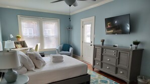 Un dormitorio con cama, mesita de noche, lámpara, cómoda, televisor y una alfombra estampada.