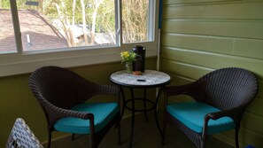 A corner room with two wicker chairs and a small table, a window with a view of trees and a building, and a green wall.