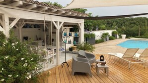Una terraza de madera con mobiliario exterior, piscina y un espacio cubierto con estanterías.
