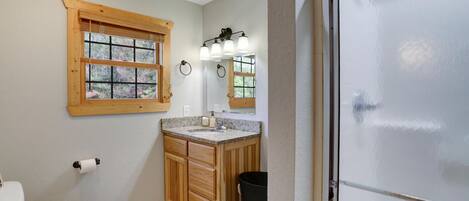 A bathroom with a toilet, wooden vanity, sink, and a window with blinds.