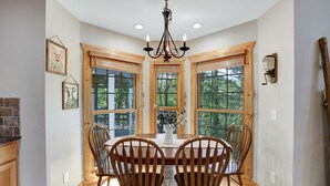 A dining area with a wooden table and chairs, large windows, and a chandelier. - NEW! Valley View Mountain Getaway (Hiawassee)