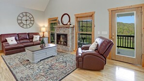 A living room with a fireplace, a leather sofa, a coffee table, and a view of a deck through a glass door. - NEW! Valley View Mountain Getaway (Hiawassee)