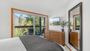 A bedroom with a large bed, a wooden dresser, a TV, and a balcony with chairs. - 3BR | Whistler Creek Ridge | Ski-in/out | Private Hot Tub | Wood Fire | Private Garage (Whistler)