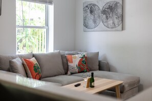Un salon moderne avec un canapé gris, des coussins colorés, une table basse en bois et une œuvre d’art représentant une carte du monde accrochée au mur.