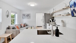 Una cocina moderna con una isla central, encimeras blancas y un lavamanos de acero inoxidable.