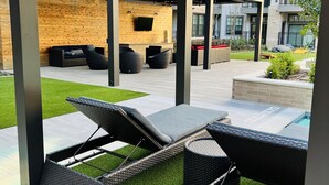 An outdoor lounge area with wicker furniture, a wooden wall, and a TV screen.