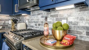 A modern kitchen with blue cabinets, a gas stove, a microwave, and a brick backsplash.