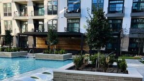 A modern apartment building with a swimming pool, outdoor seating, and a wooden deck.