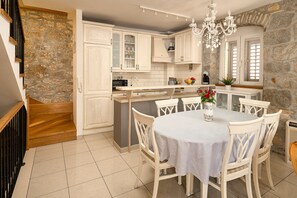 A kitchen with white cabinets, a stone wall, a dining table with chairs, and a chandelier.