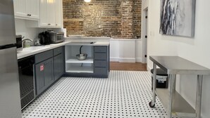 Een compacte keuken met witte kasten, een geaccentueerde bakstenen muur, een hangende lamp en een klein eiland met een spoelbak.