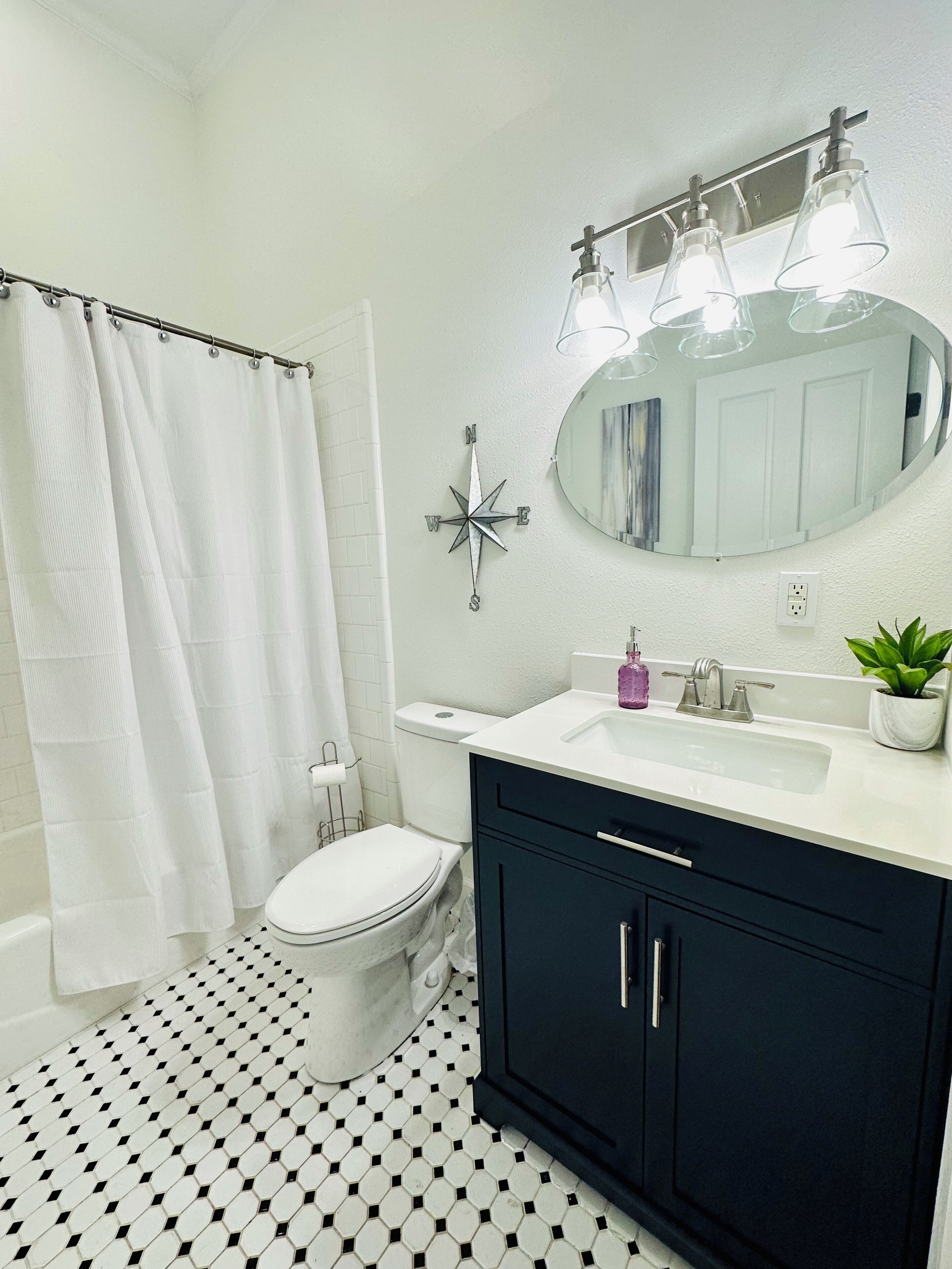 Un baño con inodoro blanco, un mueble negro, lavabo blanco, espejo y cortina de ducha.