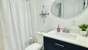 Un baño con inodoro blanco, un mueble negro, lavabo blanco, espejo y cortina de ducha.