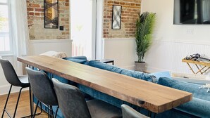 Een moderne keuken met een lange houten tafel en een bartable, een bakstenen muur en een groot raam.