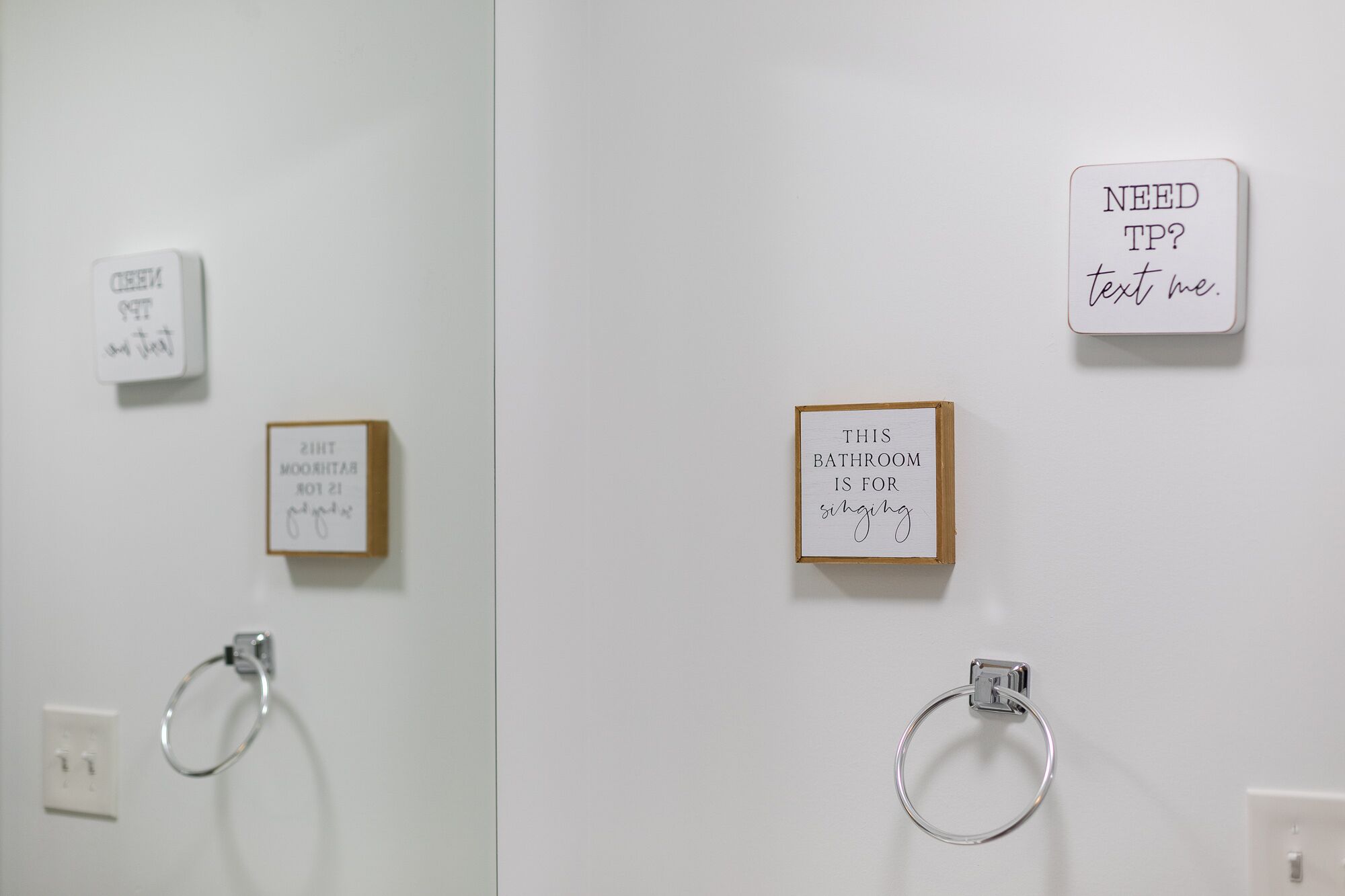 Un baño con un perchero, un cartel que dice '¿Necesitas papel higiénico? Mándame un mensaje' y un cartel que dice 'ESTE BAÑO ES PARA cantar'.