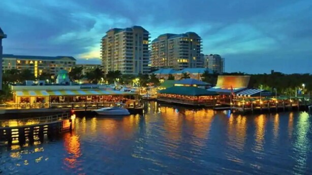 A waterfront hotel with multiple high-rise buildings, a dock with boats, and a well-lit waterfront area.