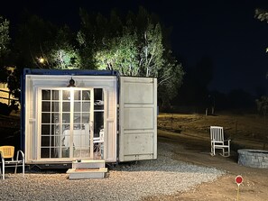 Una pequeña estructura cerrada con puerta y ventanas, un banco y una silla afuera.