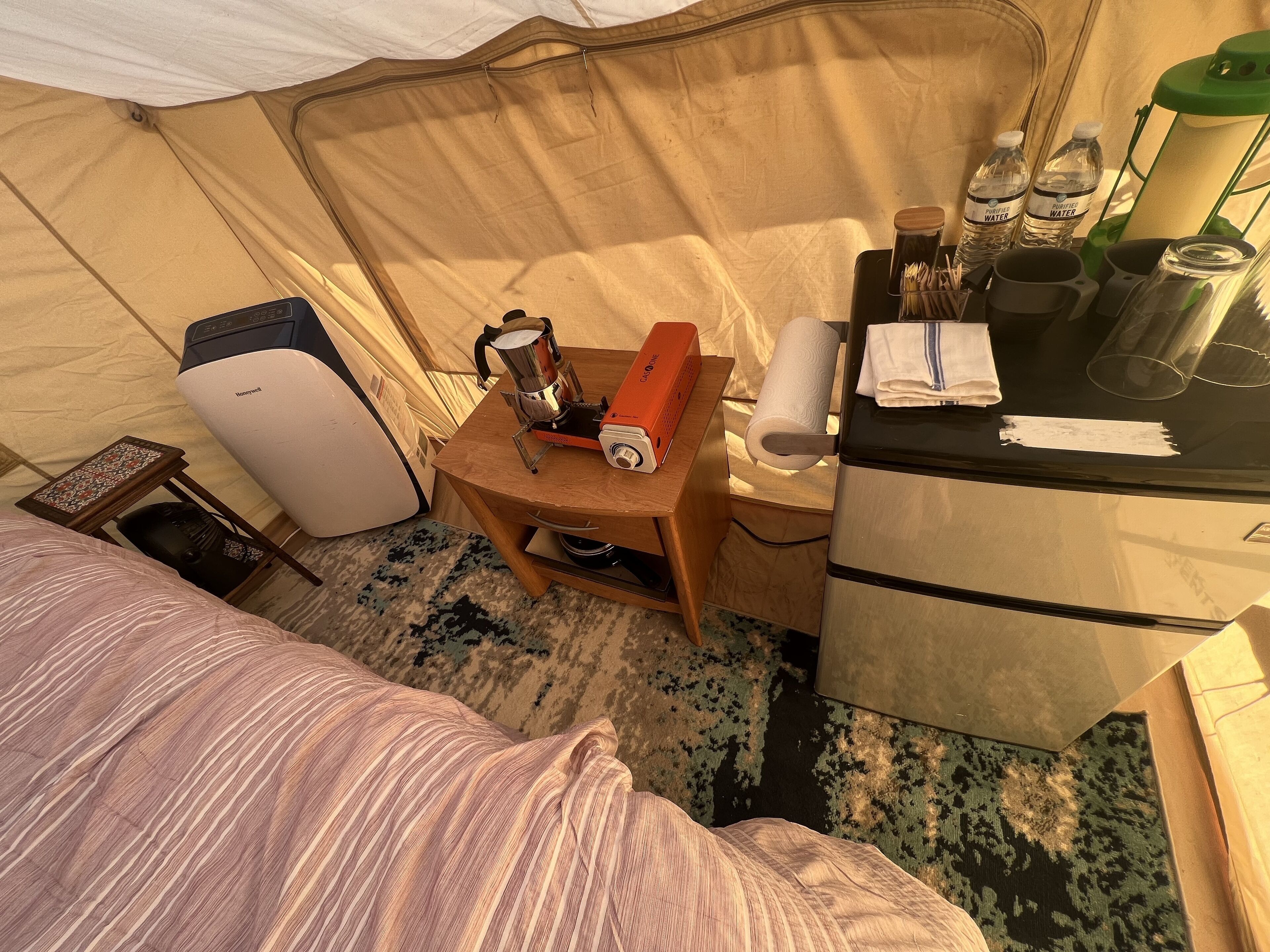 Habitación de hotel pequeña con cama, una mesita con hervidor, calefactor portátil y una botella de agua.