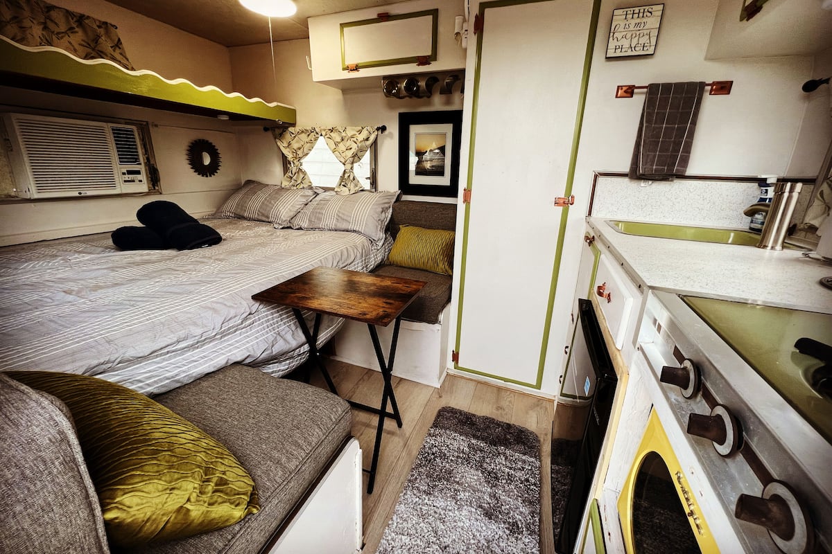 Interior de uma RV compacto e bem organizado, com cama, área de estar, cozinha compacta e um pequeno banheiro.