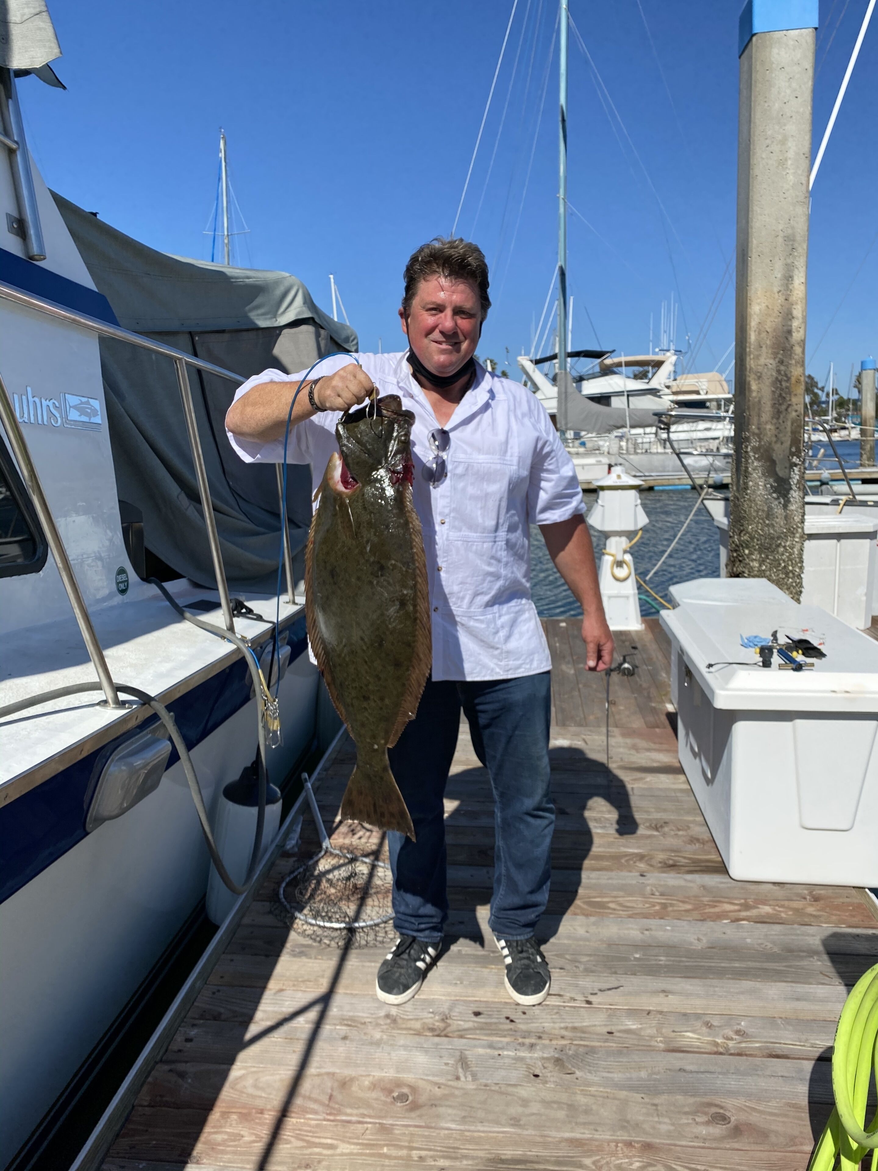 A person holding a fish on a wooden dock with boats in the background.