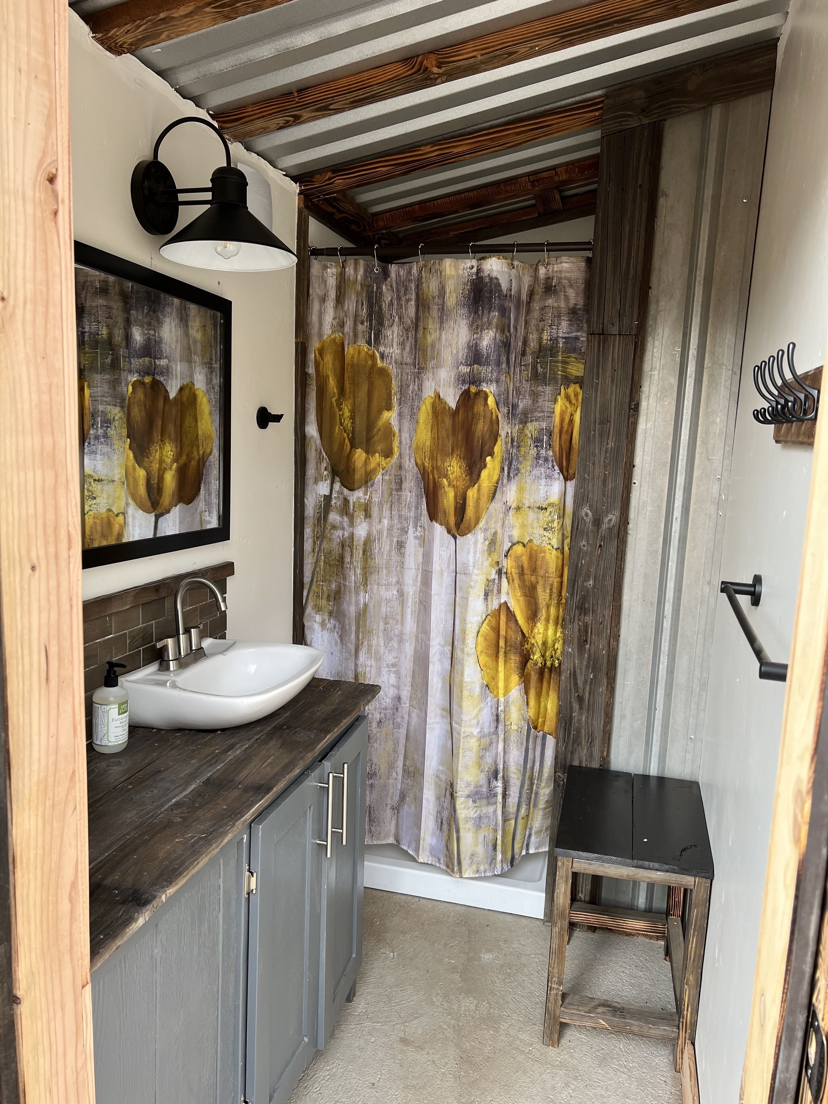 Une salle de bain avec un lavabo blanc, un meuble-lavabo en bois et un rideau de douche orné de motifs floraux.
