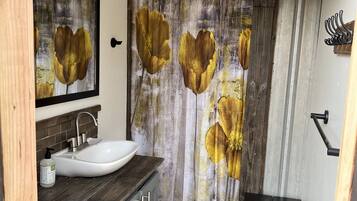 Une salle de bain avec un lavabo blanc, un meuble-lavabo en bois et un rideau de douche orné de motifs floraux.