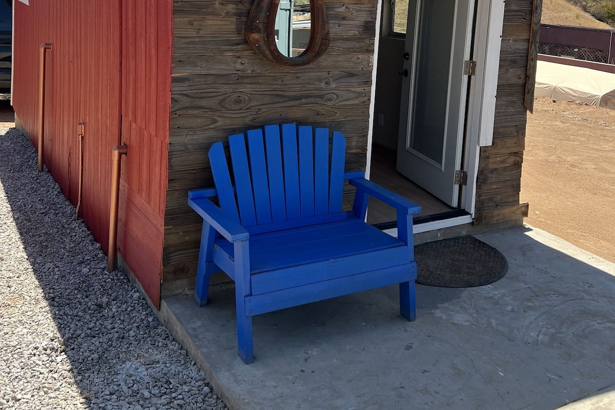 Um pequeno edifício térreo com fachada vermelha e uma cadeira Adirondack azul em frente.