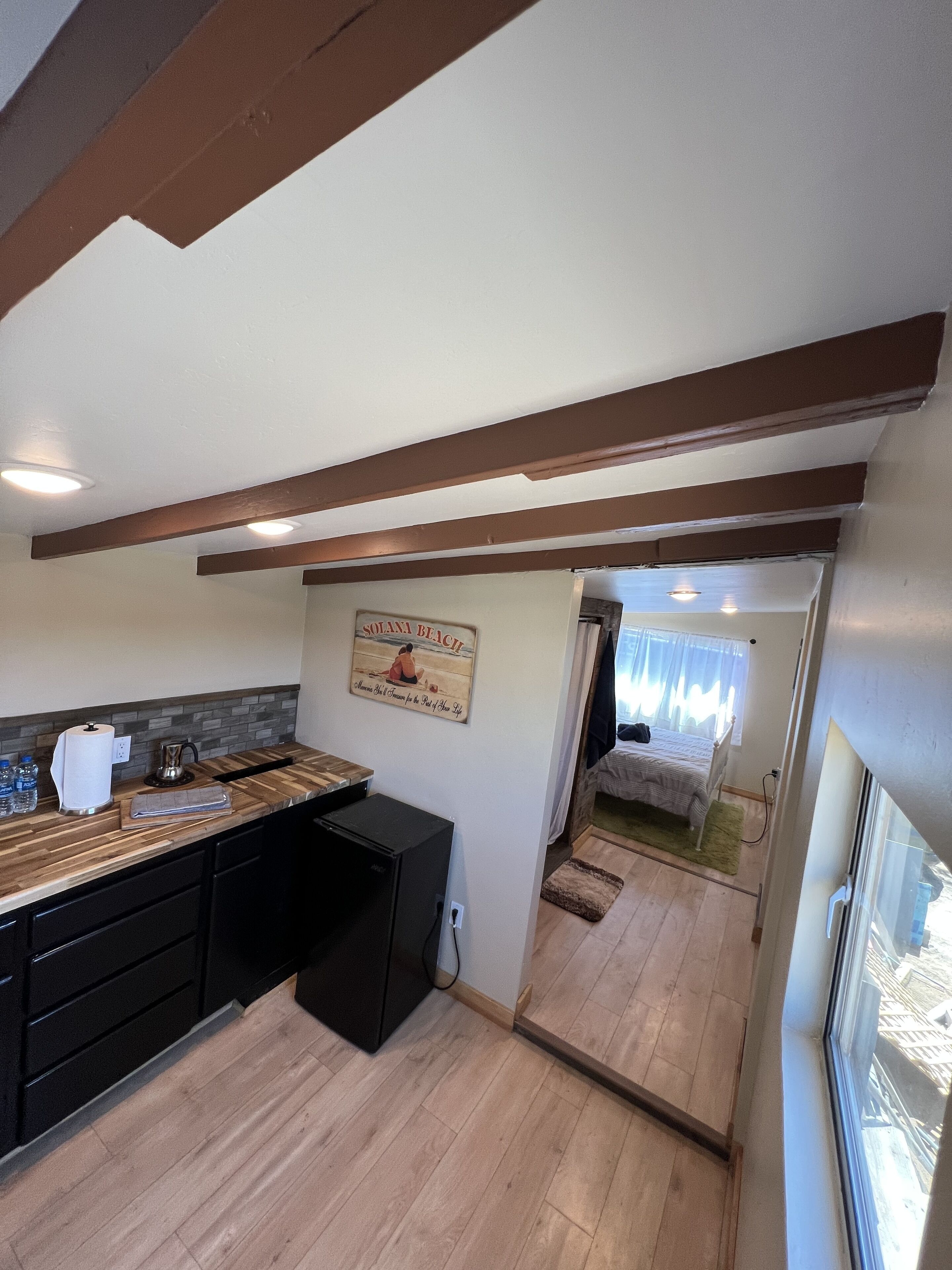 A compact kitchen with wooden countertops, a refrigerator, and a dining area. A beach-themed sign is visible on the wall.