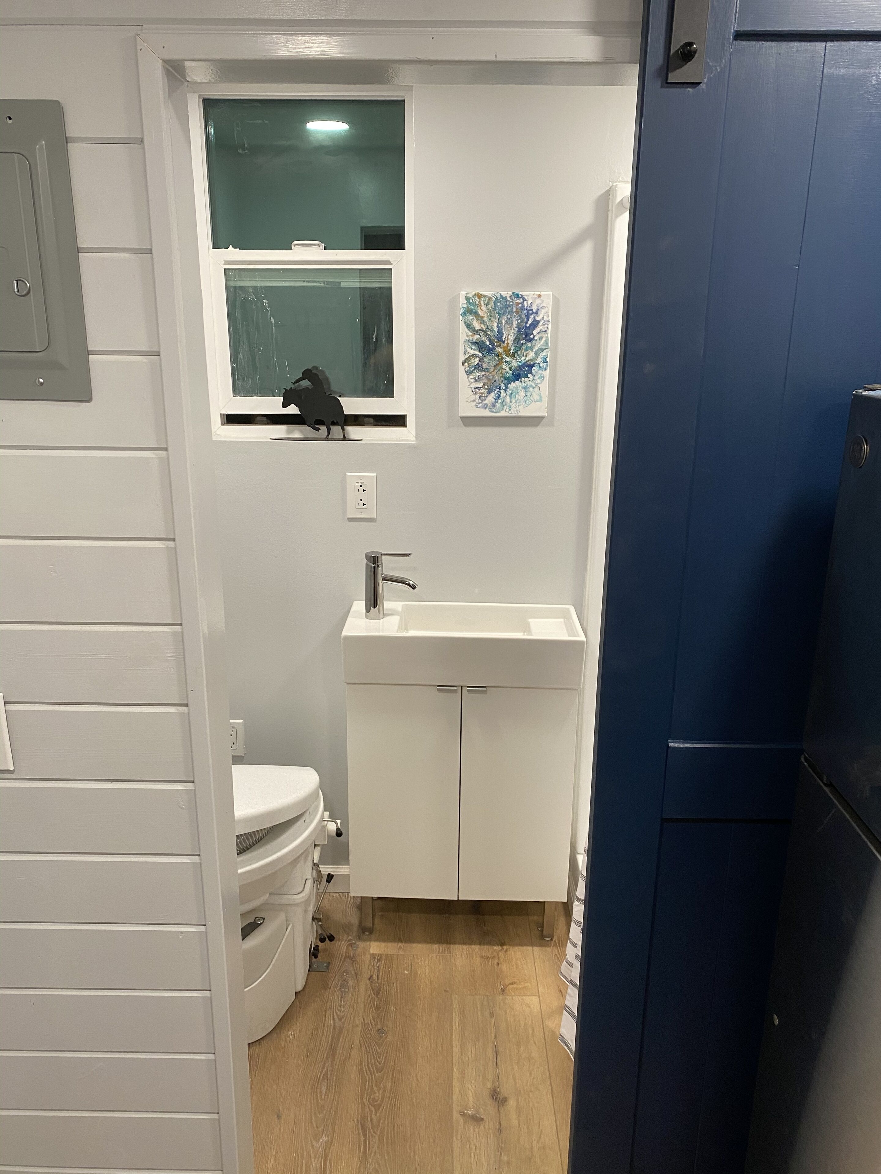 Une petite salle de bain compacte, avec des toilettes blanches, un lavabo et une fenêtre située au-dessus du lavabo.