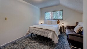 A bedroom with a bed, a window, a nightstand, a lamp, and a leather sofa. - Short Walk 2Tahoe~Family~Beach~Kings Beach Retreat (Tahoe Vista)