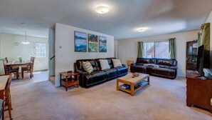 A spacious living room with a large black leather sofa, a wooden coffee table, and a dining area with a wooden table and chairs. - Short Walk 2Tahoe~Family~Beach~Kings Beach Retreat (Tahoe Vista)