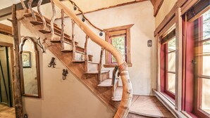 Una escalera de caracol de madera con acabado natural que conduce a un rellano con ventana de marco rojo.