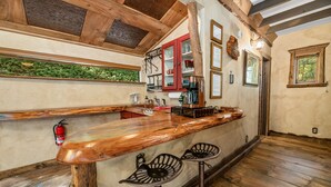 Un área de bar rústica con taburetes de madera, una barra de madera y un armario rojo con puertas de cristal.