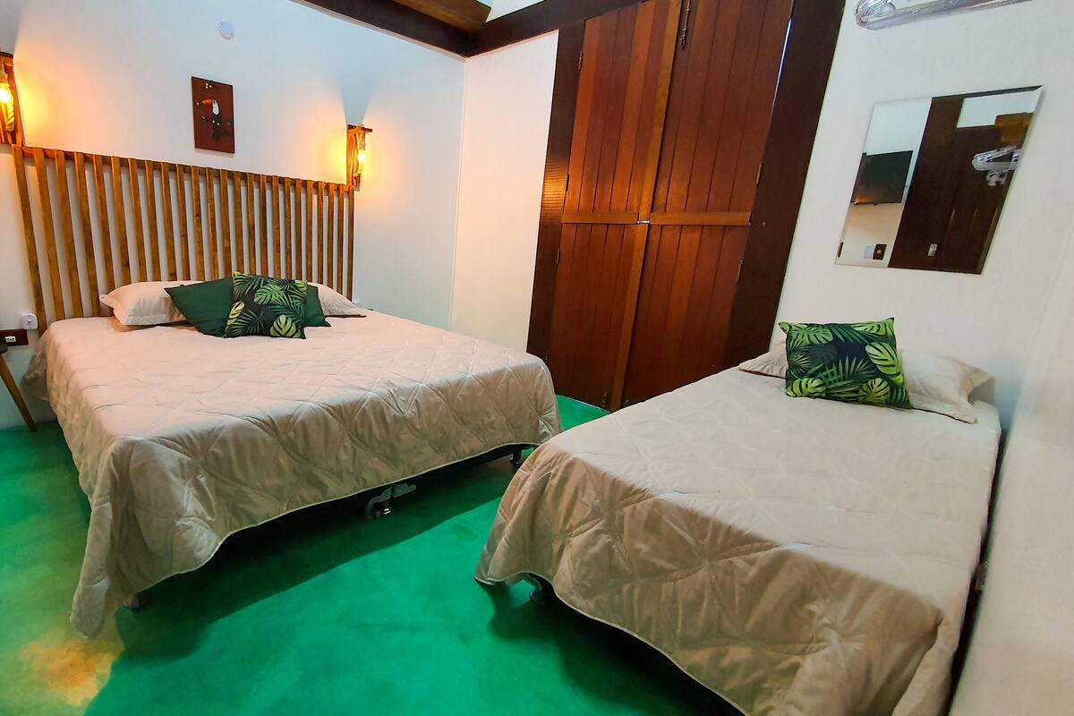 A hotel room with two beds, a wooden headboard, a small table with a plant, and a green carpet.