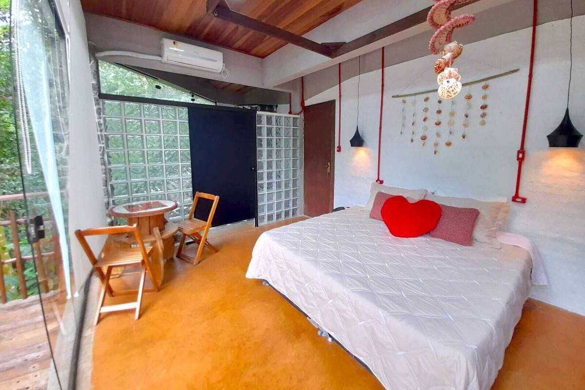 A bedroom with a large bed, a small table, and chairs, a window, and a ceiling fan.